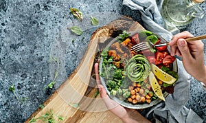 Hands holding healthy superbowl or Buddha bowl with salad, baked sweet potatoes, chickpeas, broccoli, hummus, avocado, sprouts on