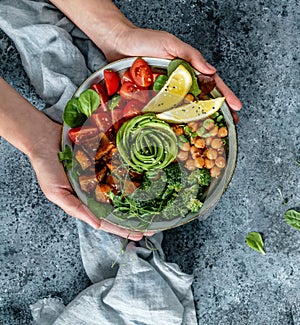 Hands holding healthy superbowl or Buddha bowl with salad, baked sweet potatoes, chickpeas, broccoli, hummus, avocado, sprouts on