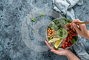 Hands holding healthy superbowl or Buddha bowl with salad, baked sweet potatoes, chickpeas, broccoli, hummus, avocado, sprouts on