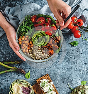 Hands holding healthy superbowl or Buddha bowl with salad, sweet potatoes, chickpeas, quinoa, tomatoes, arugula, avocado on light