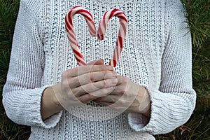 Hands holding heart made of candy cane. Woman in white sweater holding symbol of love. Christmas, Valentines day concept.