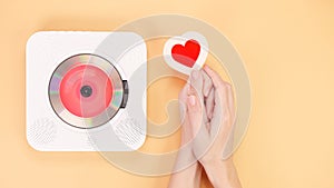 Hands holding heart shape gift card next to white cd player with red disc on