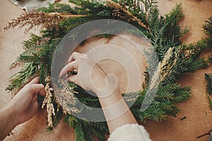 Hands holding herbs and  fir branches, pine cones, thread, berries, cinnamon on wooden table. Christmas wreath workshop. Authentic