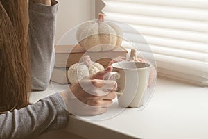 Hands holding hot cup of coffee or tea in morning sunlight, Beautiful romantic unrecognizable girl drinking hot beverage at cozy h