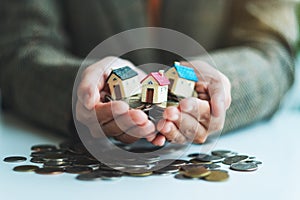 Hands holding house models and coins for saving money concept