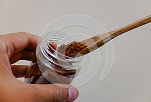 A hands holding a jar of coffee and a spoon, with cream background