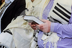 Hands holding a jewish prayer book wearing a prayer shawl