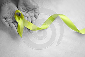 Hands holding light lime green ribbon on white fabric background with copy space. World Mental Health Day and Lymphoma Awareness