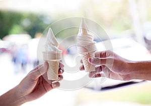 Hands holding melting ice cream waffle cone in hands on summer light nature background.