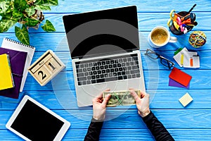 hands holding money by laptop on blue wooden table