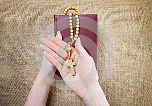 Hands holding old Holy Bible and wooden rosary