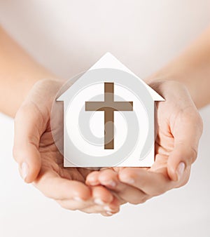 Hands holding paper house with cross symbol