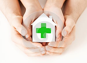 Hands holding paper house with green cross