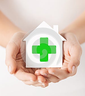 Hands holding paper house with green cross