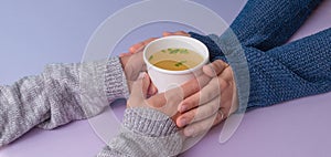 Hands holding a papern cup with broth soup