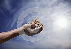 Hands holding a pile of soil with sun and sky in the background