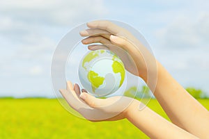 Hands holding planet earth with background of green field