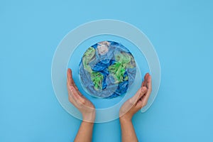 Hands holding planet Earth made from plastic disposable packages on blue background. Save the world, creative, environment