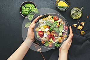 Hands holding plate with panzanella salad with stale ciabatta bread, colorful tomatoes, soft cheese, red onion, olive oil, sea