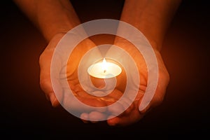 Hands holding and protecting glowing lit or burning candle candlelight on darkness