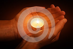 Hands holding and protecting glowing lit or burning candle candlelight on darkness