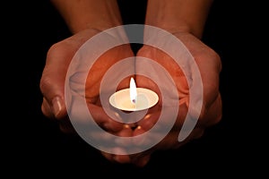 Hands holding and protecting lit or burning candle candlelight on darkness.