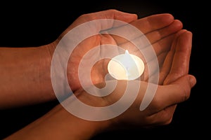 Hands holding and protecting lit or burning candle candlelight on darkness.