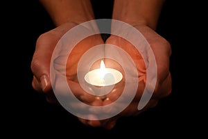 Hands holding and protecting lit or burning candle candlelight on darkness.