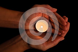 Hands holding and protecting lit or burning candle candlelight on darkness.