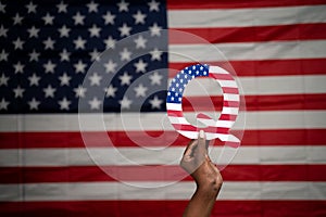 Hands holding Q alphabet with US flag as background with copy space - Concept QAnon or Q Anon deep state conspiracy theory