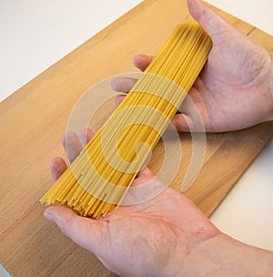 Hands holding raw, uncooked spaghetti.