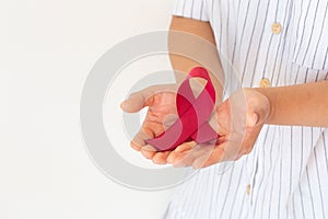 Hands holding Red burgundy ribbon bow on white background with copy space, symbol of Multiple Myeloma or Plasma cell cancer