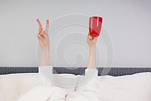 Hands holding red cup and V sign stick out under the blanket