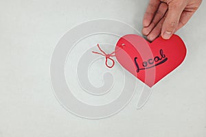 Hands holding a red heart tag with written word local. Support, promote, buy, shop and love local business concept.