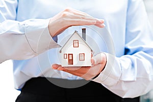 Hands holding a small house model, depicting safety and security in homeownership.