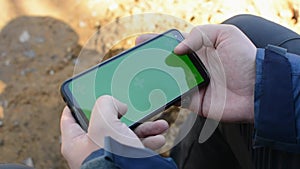 Hands holding smartphone in horizontal position touching phone with green screen