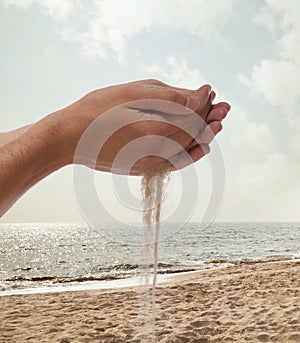 Hands holding and spilling sand with beach in the background photo