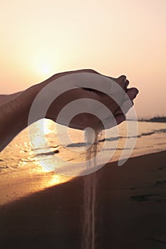 Hands holding and spilling sand with beach at sunset in the background