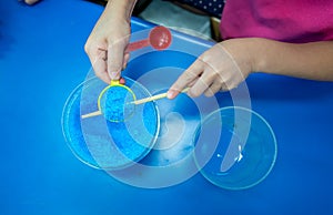 Hands holding spoon of blue chemical, Copper Sulphate Pentahydrate, against blue table