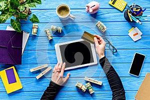 Hands holding tablet and credit card on blue wooden table with money