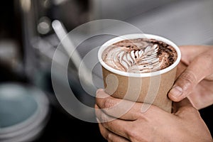 Hands holding take away cup of brewed hot coffee with Fern latte art design