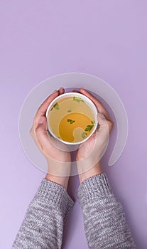 Hands holding a takeaway cup with Chicken broth soup