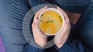 Hands holding a takeaway cup with Chicken broth soup
