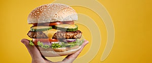 Hands holding tasty hamburger on yellow background, closeup. Space for text