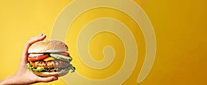 Hands holding tasty hamburger on yellow background, closeup. Space for text