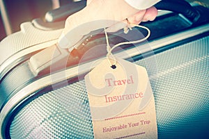 Hands holding Travel Insurance tag on Suitcase safety with letters enjoyable your trip on bag light blurred background, that is i