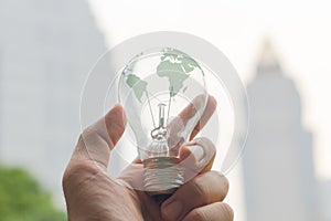 Hands holding Tungsten light bulb with green earth map