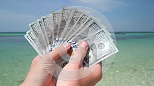 Hands holding US dollars on tropical beach. Close up