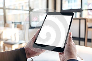 Hands holding and using black tablet pc with blank white desktop screen with notebooks on the table