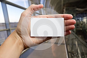 Hands holding a white business visit id card, gift, ticket, pass, present showing close up on blurred blue background